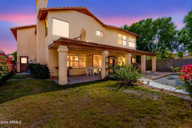 back house at dusk with a lawn, a fenced in pool, and a patio