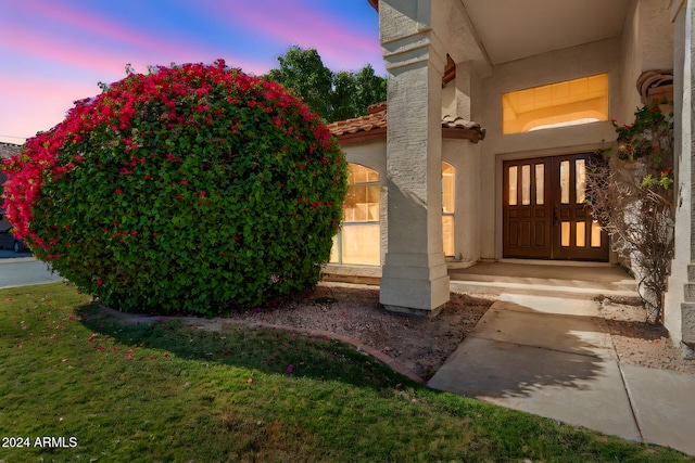 exterior entry at dusk with french doors and a lawn