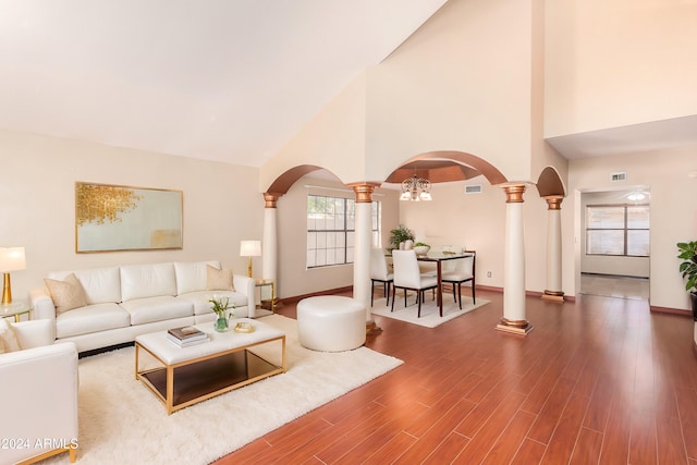 living room with wood-type flooring, ornate columns, high vaulted ceiling, and a chandelier