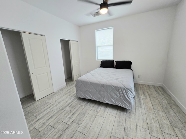 bedroom featuring visible vents, baseboards, ceiling fan, light wood-style floors, and two closets