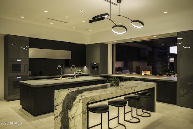 kitchen with an island with sink, a breakfast bar, pendant lighting, and sink