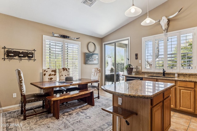 kitchen with visible vents, a kitchen island, vaulted ceiling, light stone counters, and a sink