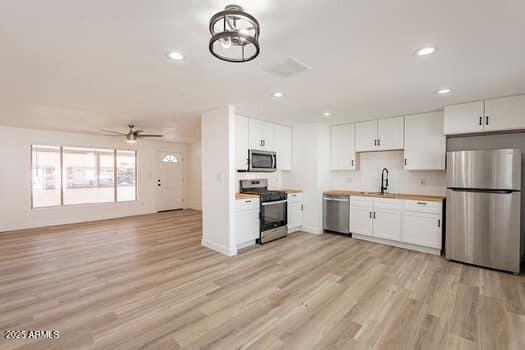 kitchen with appliances with stainless steel finishes, a sink, ceiling fan, open floor plan, and light wood-style floors