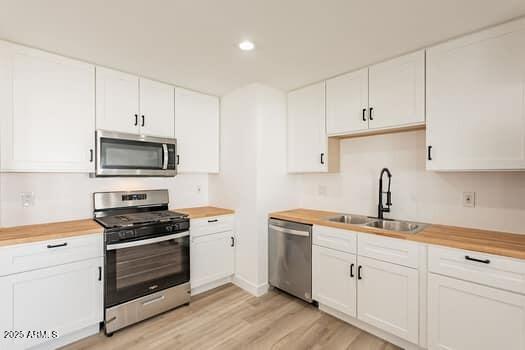 kitchen featuring appliances with stainless steel finishes, a sink, butcher block counters, white cabinetry, and recessed lighting