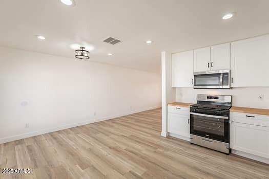 kitchen featuring appliances with stainless steel finishes, white cabinets, light wood-type flooring, wooden counters, and recessed lighting