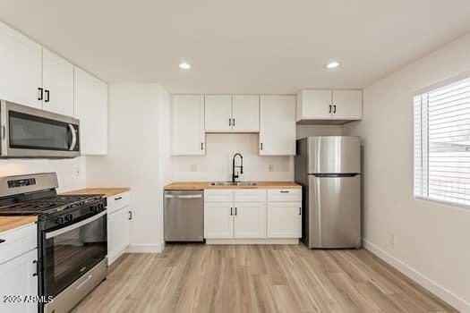 kitchen featuring appliances with stainless steel finishes, a sink, butcher block counters, light wood-style flooring, and recessed lighting