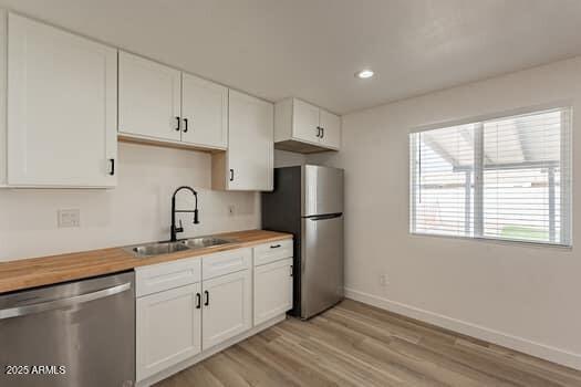 kitchen featuring stainless steel appliances, a sink, baseboards, light wood-style floors, and white cabinets
