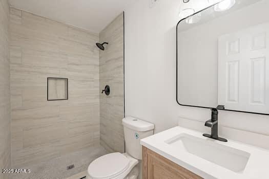 full bathroom with toilet, a tile shower, and vanity