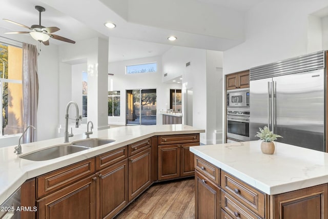 kitchen with sink, a center island, built in appliances, light stone counters, and light hardwood / wood-style floors