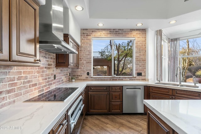 kitchen featuring stainless steel appliances, light stone countertops, sink, and wall chimney range hood