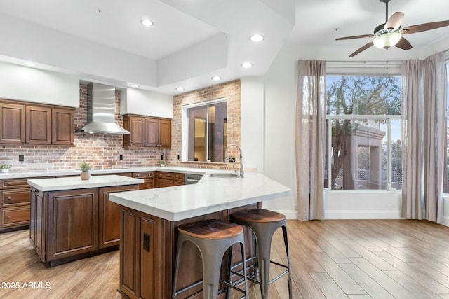 kitchen with wall chimney range hood, sink, kitchen peninsula, and light wood-type flooring