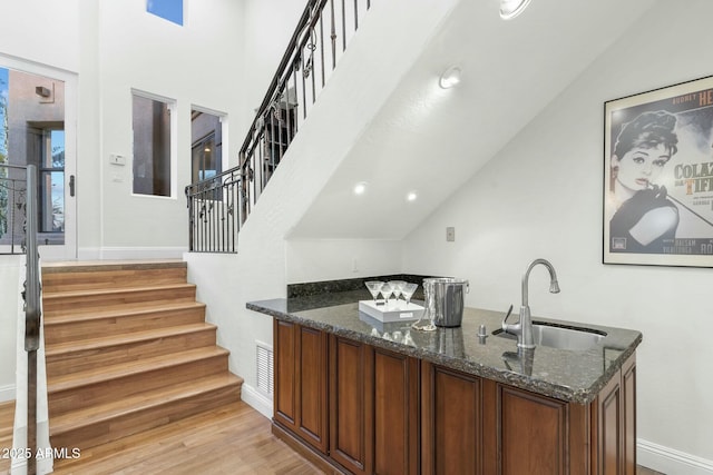 bar with sink, light wood-type flooring, and dark stone counters