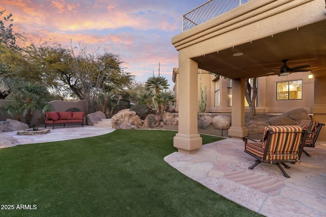 yard at dusk with an outdoor living space, a patio area, a balcony, and ceiling fan