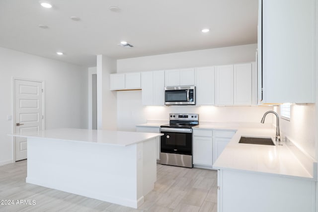 kitchen with stainless steel appliances, a kitchen island, white cabinetry, and sink