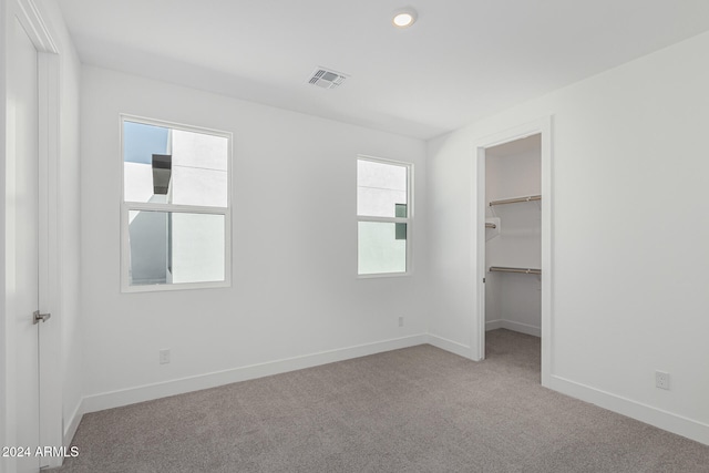 unfurnished bedroom with a closet, light carpet, and a walk in closet