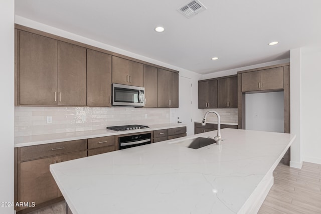 kitchen featuring light hardwood / wood-style flooring, an island with sink, stainless steel appliances, backsplash, and sink