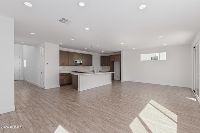 kitchen featuring decorative backsplash, dark brown cabinets, an island with sink, light hardwood / wood-style floors, and sink