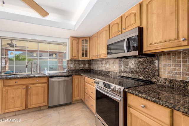 kitchen with appliances with stainless steel finishes, tasteful backsplash, ceiling fan, dark stone counters, and sink