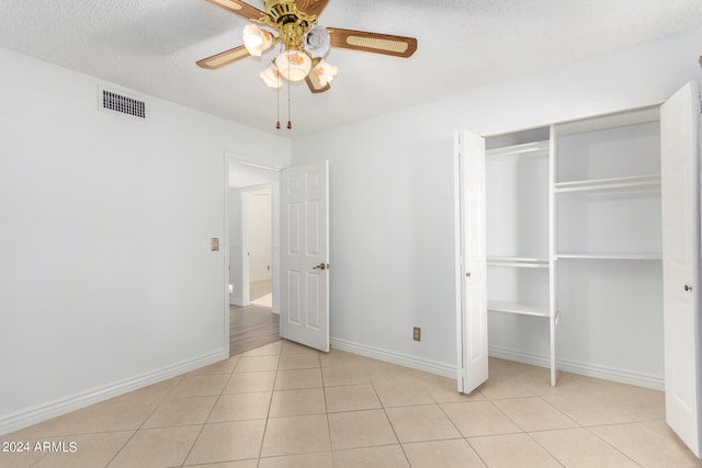 unfurnished bedroom with a textured ceiling, light tile patterned floors, ceiling fan, and a closet