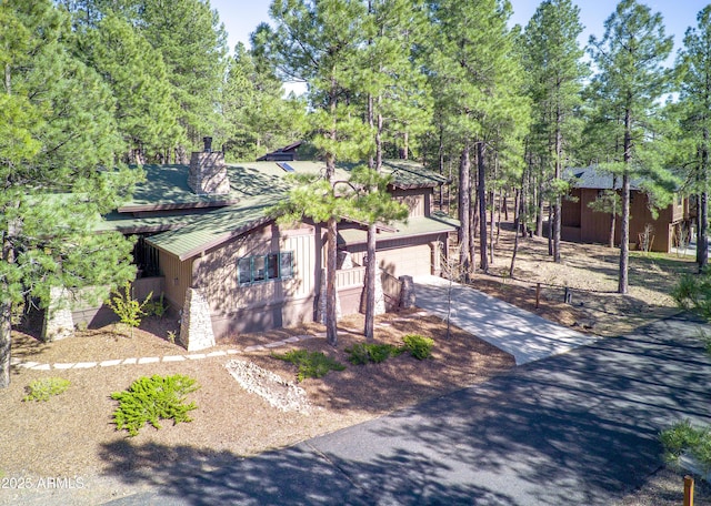 view of front of house featuring concrete driveway, metal roof, a chimney, an attached garage, and view of wooded area