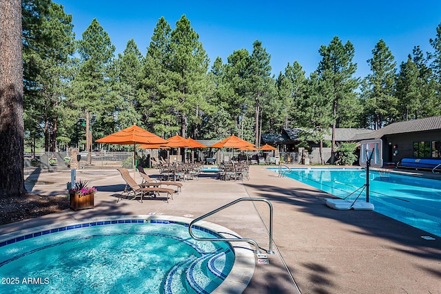 community pool featuring fence, a patio, view of wooded area, and a community hot tub
