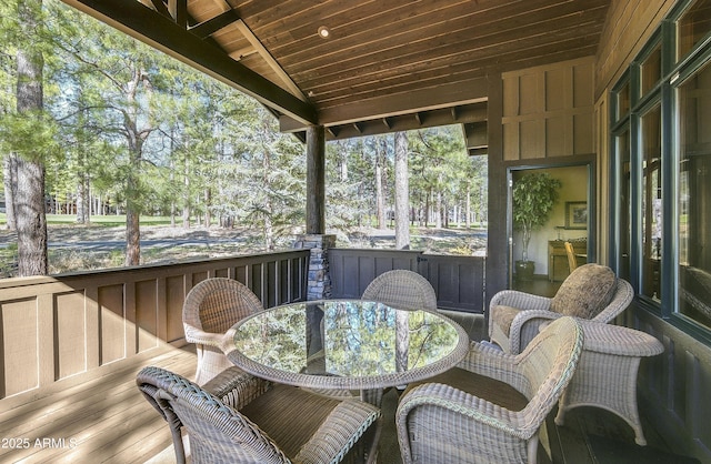 sunroom / solarium featuring outdoor dining area, lofted ceiling, and view of scattered trees