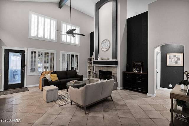 tiled living room featuring a tiled fireplace, ceiling fan, a healthy amount of sunlight, and beam ceiling