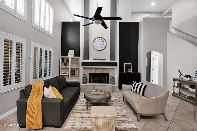 living room with light tile patterned flooring, ceiling fan, a tile fireplace, and a towering ceiling