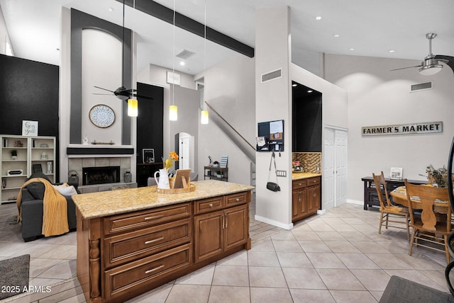 kitchen with a tile fireplace, light stone countertops, light tile patterned floors, and ceiling fan