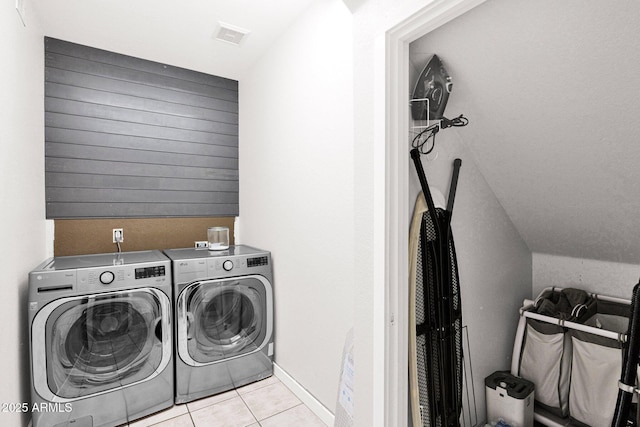 clothes washing area with washing machine and dryer, light tile patterned flooring, and wooden walls