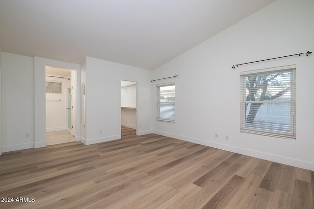 unfurnished bedroom with hardwood / wood-style floors, a spacious closet, multiple windows, and vaulted ceiling