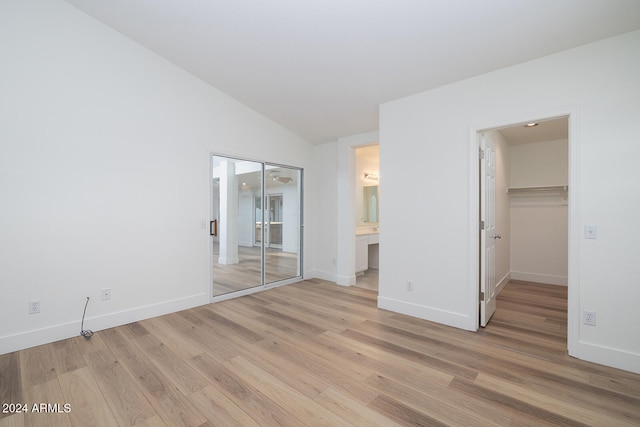 unfurnished bedroom featuring ensuite bathroom, vaulted ceiling, and light hardwood / wood-style flooring