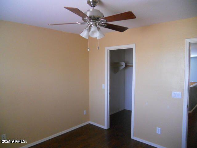 unfurnished bedroom with ceiling fan, a closet, dark hardwood / wood-style floors, and a walk in closet