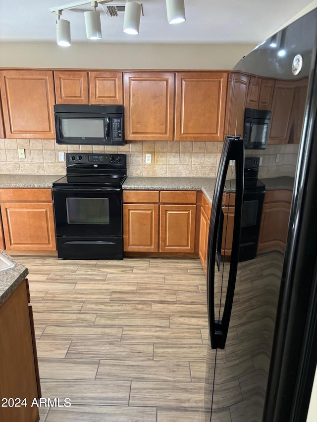 kitchen with light stone counters, light hardwood / wood-style floors, decorative backsplash, and black appliances