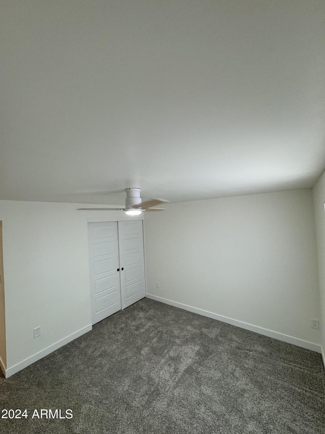 unfurnished bedroom featuring vaulted ceiling, dark colored carpet, and ceiling fan