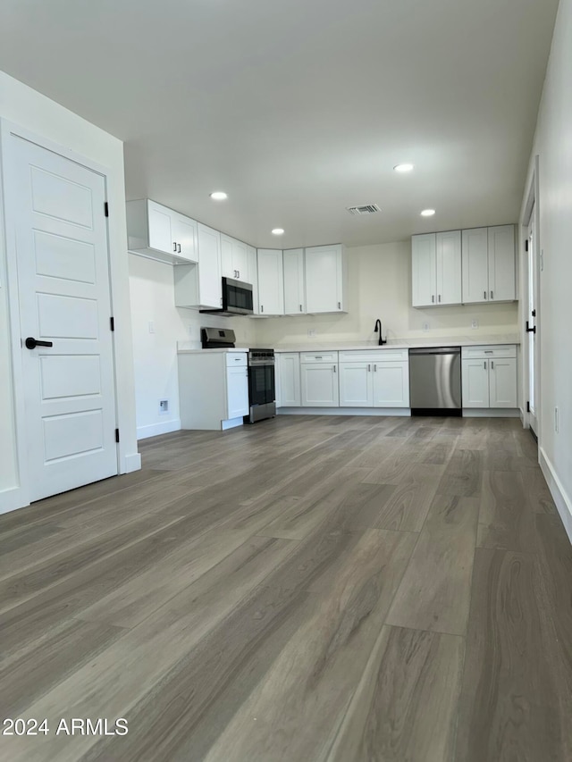 kitchen with sink, appliances with stainless steel finishes, white cabinetry, and light hardwood / wood-style floors