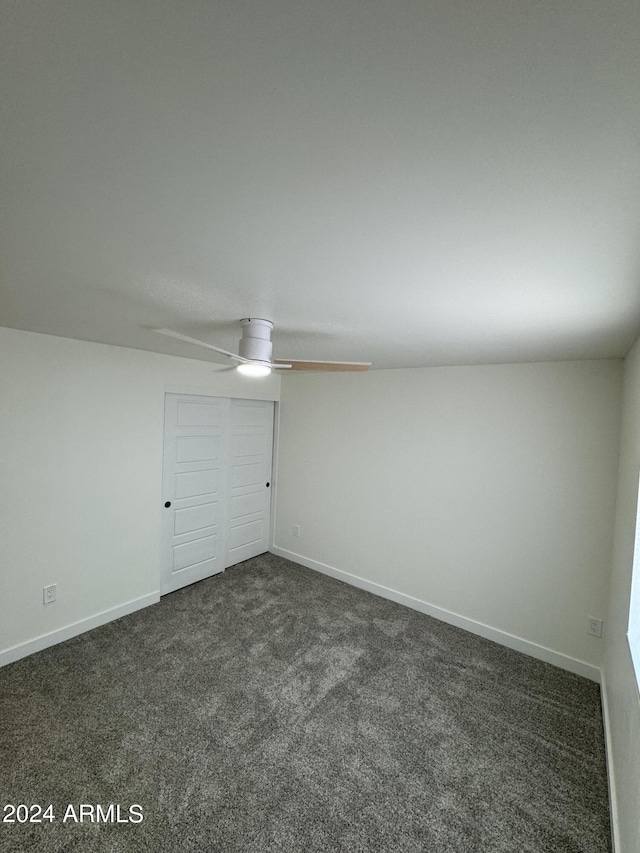 unfurnished bedroom with dark carpet, a closet, and ceiling fan