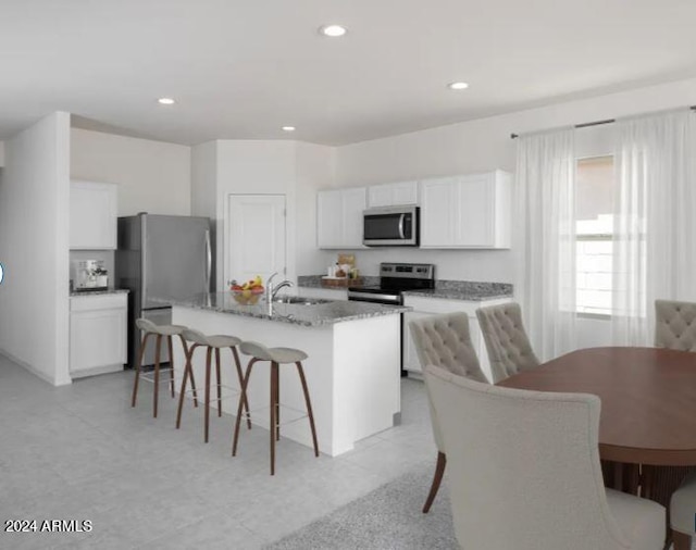 kitchen featuring white cabinets, a kitchen island with sink, appliances with stainless steel finishes, a kitchen breakfast bar, and light stone countertops