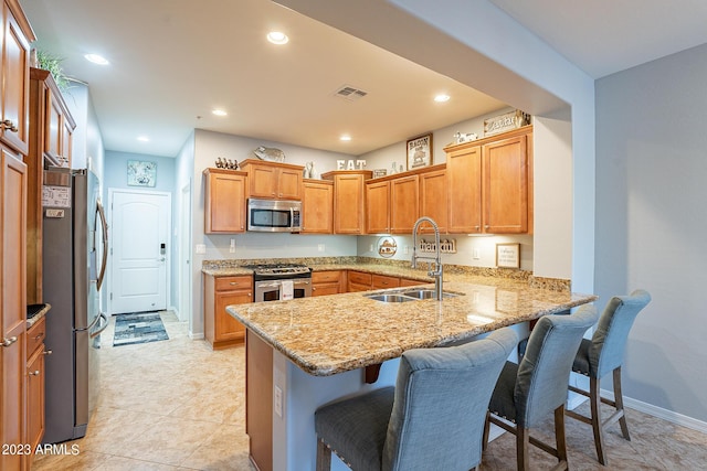 kitchen featuring sink, a breakfast bar area, stainless steel appliances, light stone counters, and kitchen peninsula