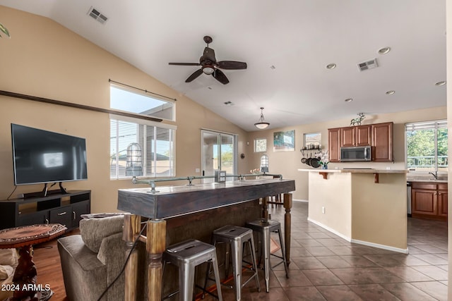 kitchen with lofted ceiling, dark tile patterned flooring, ceiling fan, a healthy amount of sunlight, and a breakfast bar area