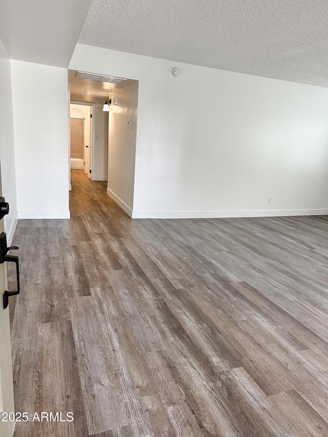 spare room featuring a textured ceiling, baseboards, and wood finished floors