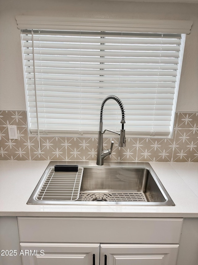 details featuring backsplash, white cabinetry, light countertops, and a sink