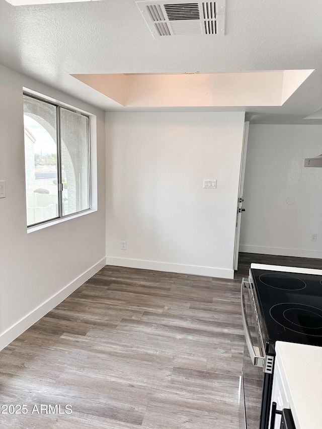 interior space with a textured ceiling, wood finished floors, visible vents, baseboards, and a raised ceiling