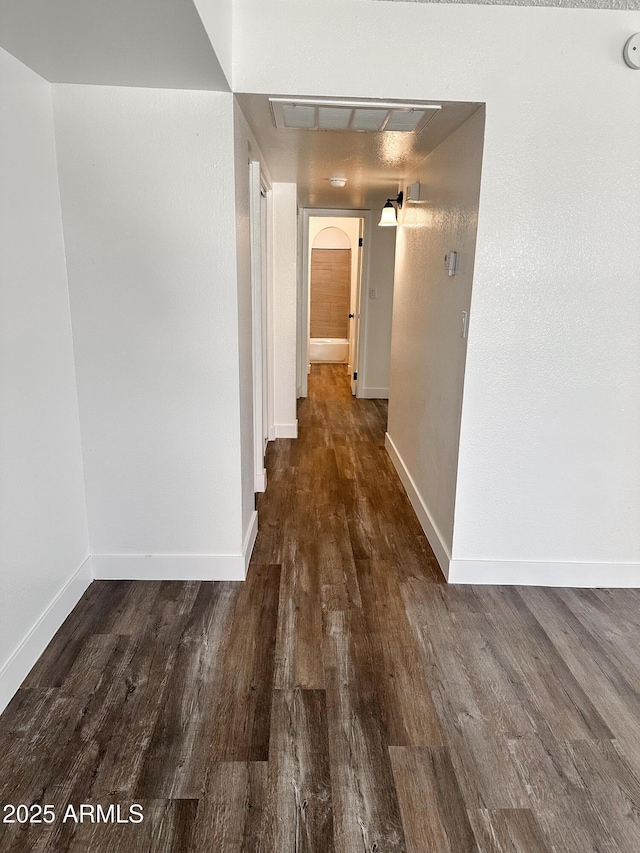 hallway featuring arched walkways, dark wood-type flooring, visible vents, and baseboards