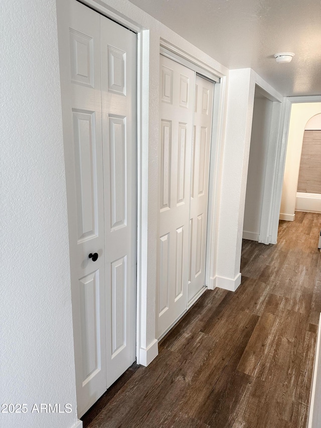 hallway featuring baseboards, arched walkways, dark wood finished floors, and a textured wall