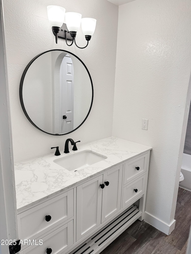 full bathroom featuring a tub, vanity, baseboards, and wood finished floors