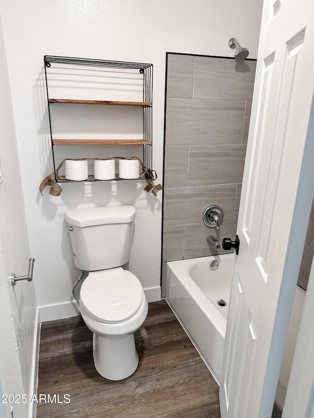 bathroom with toilet, baseboards,  shower combination, and wood finished floors