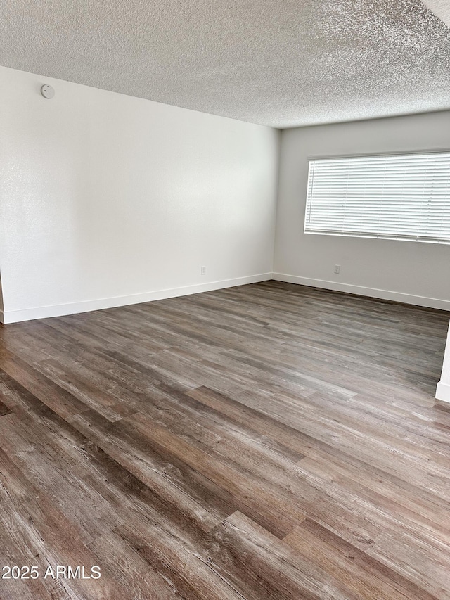 spare room featuring a textured ceiling, dark wood-type flooring, and baseboards