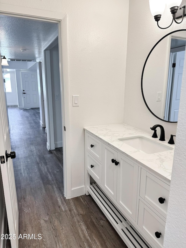 bathroom featuring a textured wall, a textured ceiling, vanity, wood finished floors, and baseboards