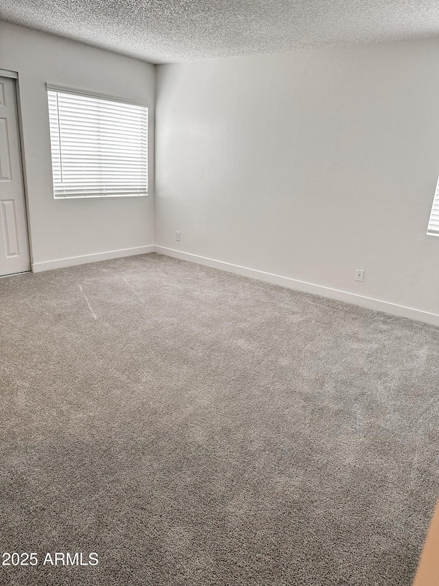 empty room featuring a textured ceiling, carpet, and baseboards